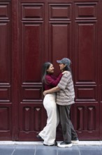 A loving moment between latin lesbian couple, embracing in front of a deep maroon door. The image