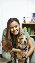 A nutritionist smiles warmly, embracing a beagle in an office setting. Shelves with nutritional