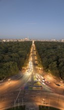 An aerial view of Berlin's Strabe des 17 Juni at dusk, featuring a tree-lined boulevard illuminated