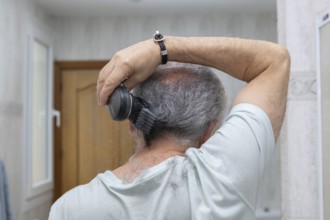 A man using an electric clipper to trim his hair in a home bathroom setting. The image captures the