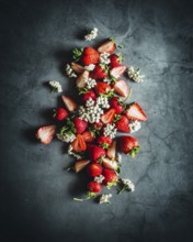 A visually striking arrangement of ripe strawberries beautifully scattered on a dark stone surface,