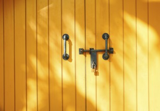 Yellow wooden door in California, USA, featuring strong metal handles and a padlock. Sunlight casts