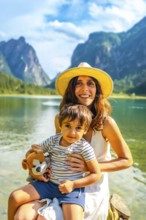 Mother holding her son while enjoying a sunny summer day at lake dobbiaco with the dolomites in the