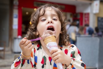 A young girl delights in a chocolate ice cream cone, savoring every bite on a sunny day in a