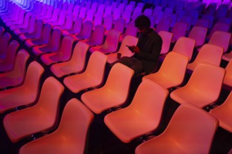 A indian man sits among vibrant, colorful auditorium chairs at a conference of AI in Amsterdam