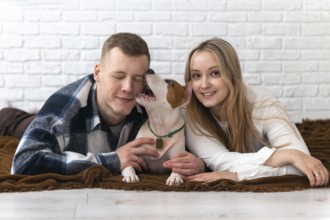 A young couple shares a loving moment with their energetic white and brown dog, lying on a cozy