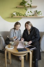 Two women engage in a collaborative discussion at a cozy cafe, using a tablet. They sit at a wooden