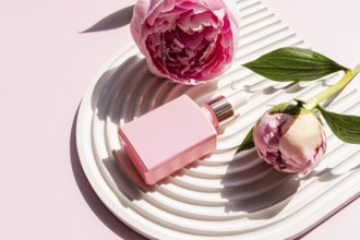 A pink cosmetic bottle is elegantly placed on a white decorative tray, surrounded by beautiful pink
