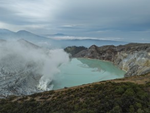 Drone view of Ijen crater in Indonesia with turquoise acidic lake and visible sulfur smoke near the