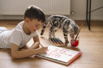 A boy lies on the floor, drawing a Mother's Day card with vibrant paints. His dedicated expression