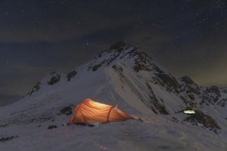 A glowing tent in a snowy mountain landscape under a starlit sky. Perfect for ski touring and