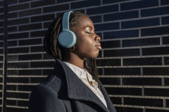 An African American businesswoman with braids enjoys a break, listening to music through