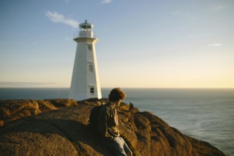 Side view of unrecognizable young man sitting on rocks gazing at the ocean near Cape Spear