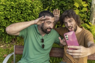 Two friends have fun taking a playful selfie while sitting on a park bench The man in green, who is