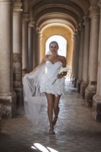 A bride in a stunning white gown gracefully walks down the aisle of the ancient villa in Treia,