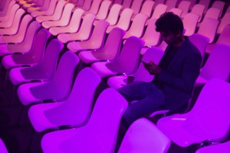 Indian man at a conference of AI in Amsterdam sits amid rows of vibrant purple lit chairs, deeply