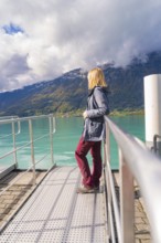 Woman in casual clothes leaning on the railing of a jetty with a view of the lake and mountains,