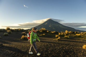 A woman hiker walks through the rugged terrain near Mount Taranaki, New Zealand, as the sun rises,