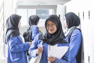 A group of Muslim students in blue uniforms and hijabs gathers in a school hallway, symbolizing