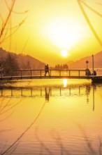 People on a bridge over a lake at sunset with intensive reflection, Großer Alpsee, Immenstadt im