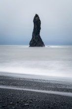 A dramatic sea stack rises from the ocean at Reynisfjara Beach in Iceland, surrounded by mist and