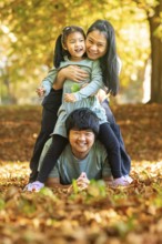 Asian family enjoying a playful moment outdoors in an autumn park. The child rides on the father's