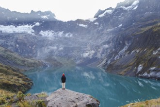 An Ecuadorian woman stands on a rocky ledge, overlooking the serene turquoise waters and majestic