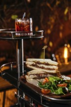 A gourmet setting features a stacked club sandwich with veal cheeks, cheese, and fresh greens,