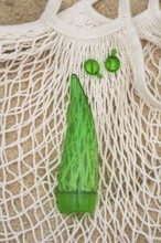 Top view of a green aloe vera gel tube and two green capsules placed on a white net bag, set