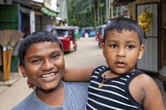 Two young boys pose happily on a street, one smiling, the other seriously, A family in Ratnapura in