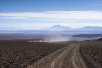 A dusty, gravel road cuts through the arid landscape of La Puna in Argentina, offering a view of