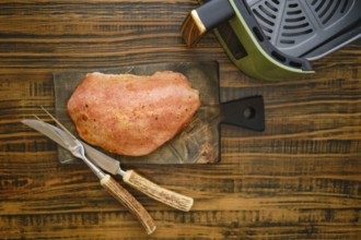 A piece of roasted pork meat on a wooden cutting board. Kitchen knife and fork are placed next to