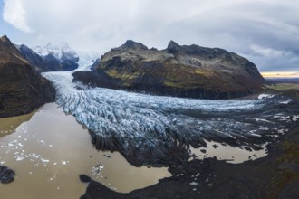 A panoramic shot of the vast Vatnajökull Glacier flowing between rugged mountains under a cloudy