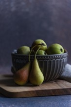 A collection of fresh wild pears displayed in a decorative ceramic bowl, resting on a wooden board.