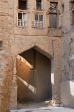 A textured, sunlit archway casts golden hues across the crumbling facades of traditional mud-brick