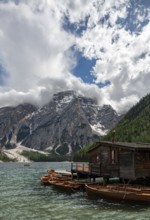 Traditional wooden rowboats rest near a rustic wooden boathouse on Lago di Braies, surrounded by