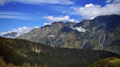 Wide mountain landscape under blue sky surrounded by clouds, Stepantsminda, Caucasus, Georgia