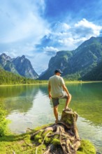 Tourist standing on a tree stump admires the breathtaking landscape of lake dobbiaco, surrounded by