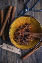 Top view of a rustic yellow bowl filled with star anise and cinnamon sticks, accompanied by a pair