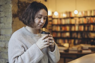 A woman in a soft sweater holds a takeaway coffee cup while enjoying a peaceful moment in a cozy