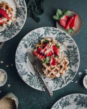 Delicious waffles topped with fresh strawberries and cream are elegantly served on beautiful