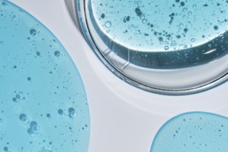 A close-up image of vibrant blue cosmetic gel droplets with visible texture and bubbles, set