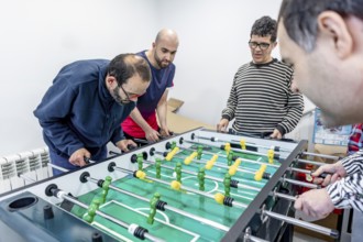 A group of people enjoy a friendly game of foosball at a mental health residence. The activity