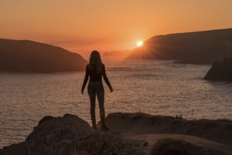 A silhouette of a woman stands on a rocky cliff at Arnia Beach, Costa Quebrada, gazing toward the