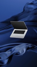 A sleek laptop is placed atop smooth fabric, showcasing its lightweight design against a rich blue