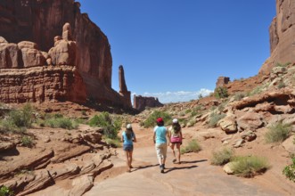 Three people hiking in a vast desert landscape with impressive red rock formations, Arches National
