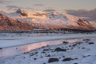 Majestic Icelandic landscape with sunset hues on snow-covered peaks, reflected in icy waters. A