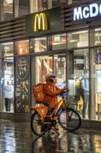 Street at the main station, Lieferando courier, cyclist, rainy weather, city centre, in the