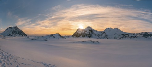 The sun sets behind the rugged, snow-covered peaks of Katla Glacier, casting a golden glow over the