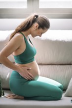 A pregnant woman wearing a green yoga outfit is practicing wellness and mindfulness in a serene